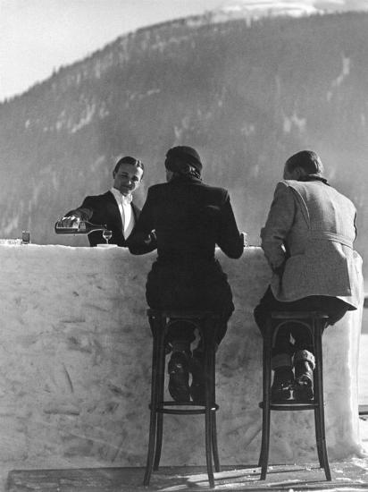 British Couple on High Stools at Ice Bar Outdoors at Grand Hotel as Waiter Pours Them Drinks